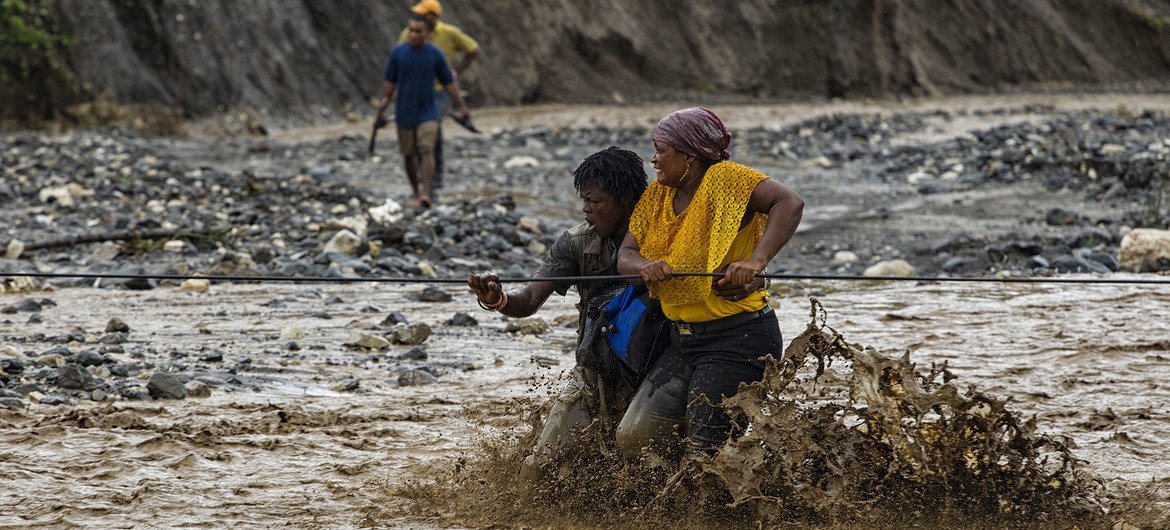 People cross a flooded river in Haiti with the help of a rope and porters after the bridge was washed away by Hurricane Matthew. Photo Logan Abassi UN/MINUSTAH