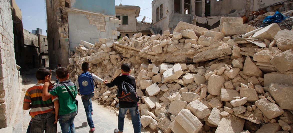 Children walk by houses destroyed by on-going fighting after their first day of school in eastern Aleppo, Syria.