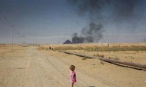 A young internally displaced Iraqi girl stands on a dusty path at the edge of Debaga camp, near Mosul in northern Iraq. Smoke from oil fires can be seen in the background.