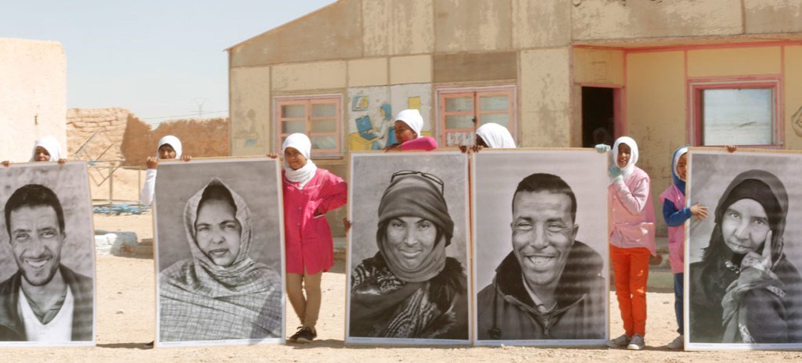 Des réfugiés du Sahara occidental avec des portraits à l'extérieur du camp de réfuiés de Smara, près de Tindouf, en Algérie. Photo ONU/Evan Schneider