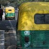 Rear view of a yellow and green auto rickshaw on a street in Delhi, India.