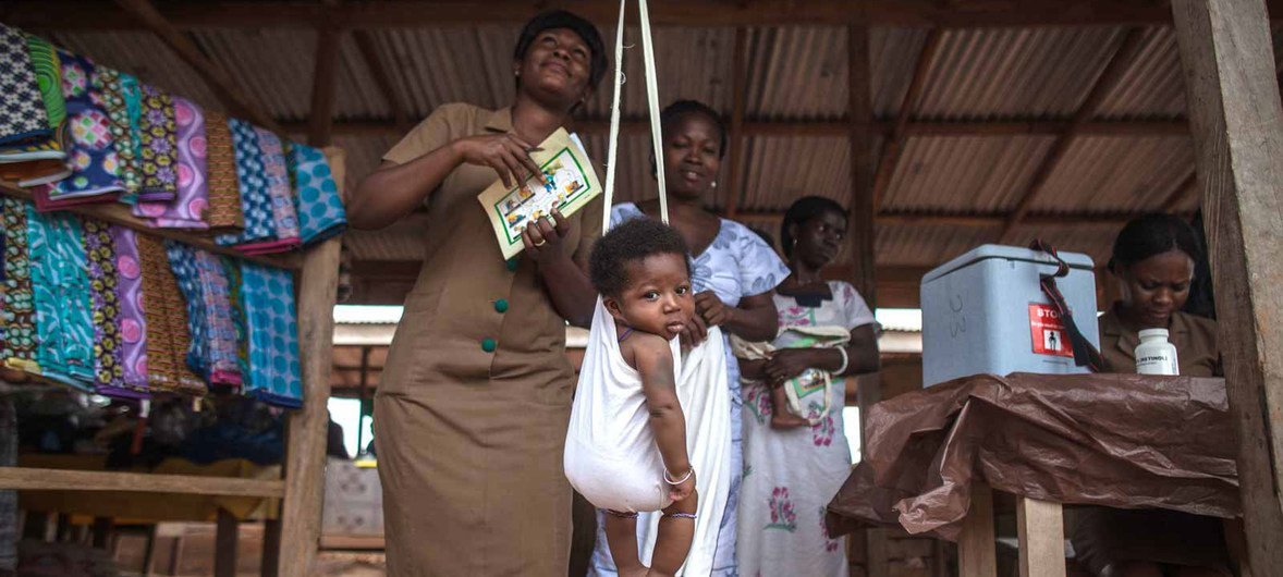 在加纳，一名社区卫生工作者在接种疫苗之前给一名婴儿称体重。 2012年，加纳成为非洲第一个同时引入肺炎球菌病和轮状病毒疫苗的国家，以应对世界上主要的两种致命儿童疾病：肺炎和腹泻。