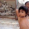 Two young children stand next to a cage filled with skulls at a memorial site in Cambodia.