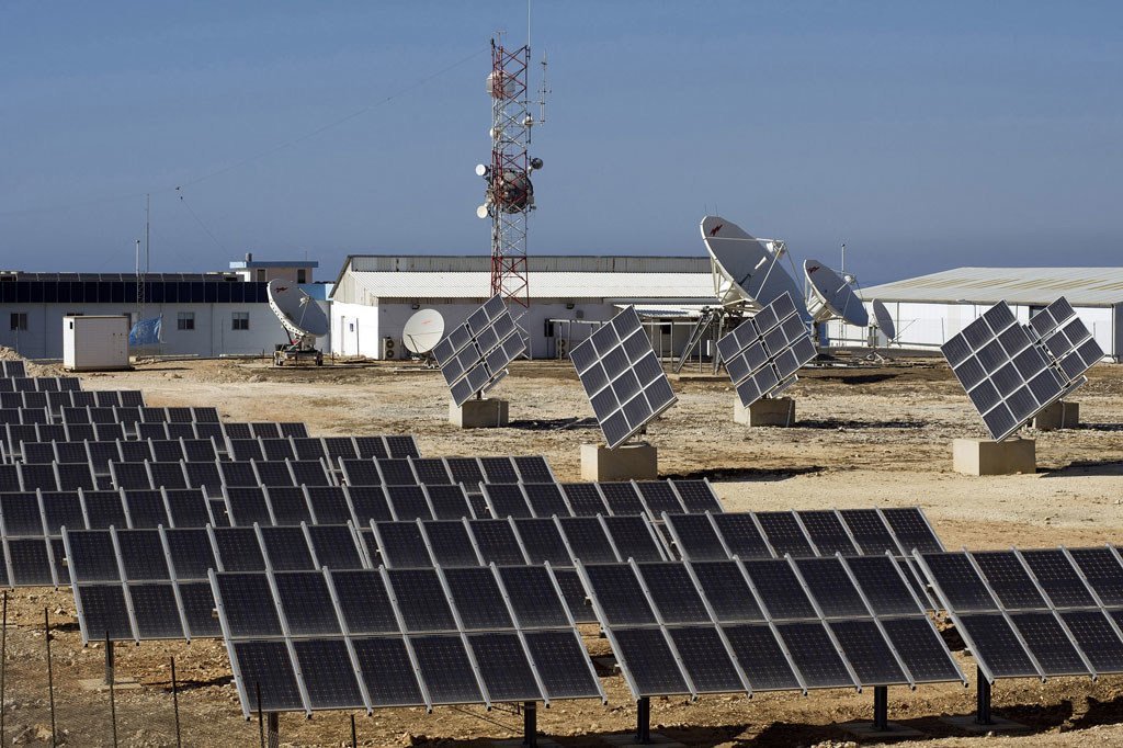 Rows of solar panels and satellite dishes at a UNIFIL base in a desert setting.