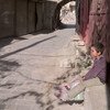 一个九岁男孩坐在阿勒坡老城的墙边，他手里拿着一个水罐，希望找到水喝。儿基会图片 Zayat