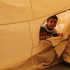 Two young Iraqi boys, their family displaced by the fighting in Mosul, peek out through the zipper of their tent at Hasansham camp, as UNHCR delivers cold weather supplies, including warm blankets and stoves.