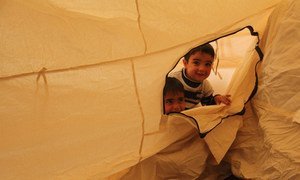 Two young Iraqi boys, their family displaced by the fighting in Mosul, peek out through the zipper of their tent at Hasansham camp, as UNHCR delivers cold weather supplies, including warm blankets and stoves.