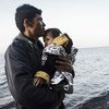 अफ़ग़ानिस्तान में एक युवा शरणार्थी अपने छोटे बच्चे को गोद में लिये हुए, तुर्की से सुरक्षित लेस्बोस द्वीप पर पहुँचने के बाद.