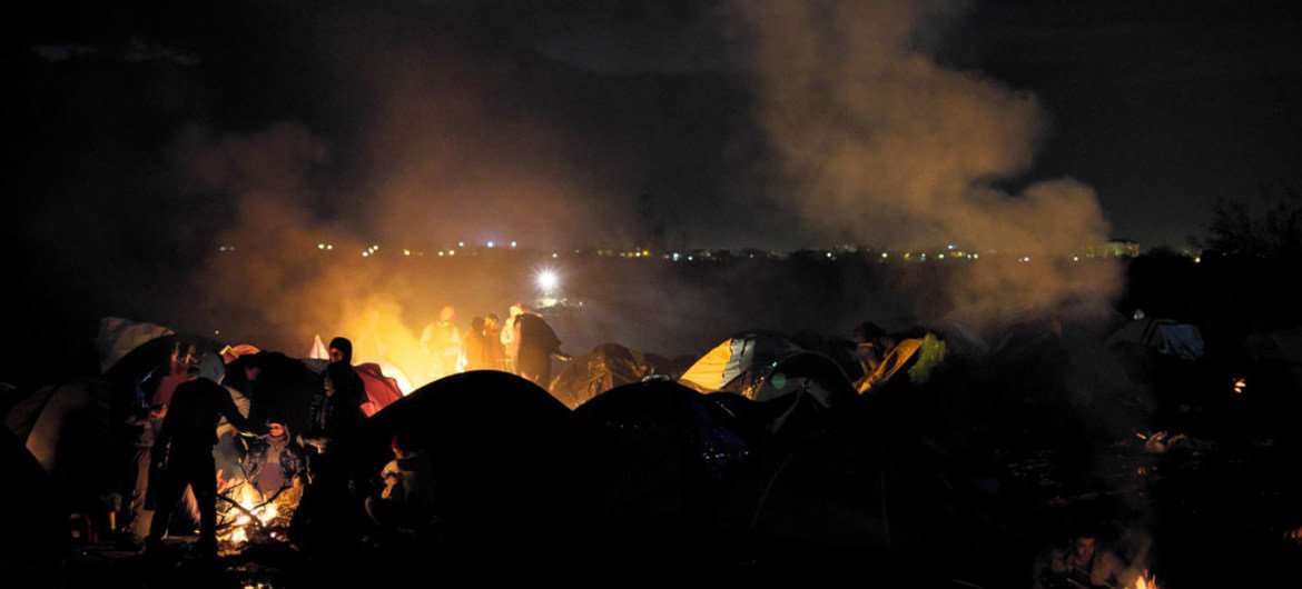 Refugees and migrants warm themselves at various fires at nightfall, outside tents in an area near the town of Idomeni, Greece.