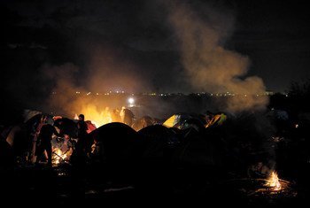 Refugees and migrants warm themselves at various fires at nightfall, outside tents in an area near the town of Idomeni, Greece.