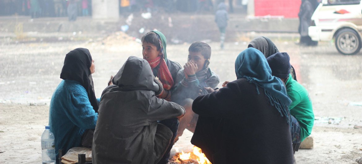 Children and their parents gather around a fire to keep warm in the yard of a large warehouse in Jibreen, now used as a shelter for thousands of families who fled violence in eastern Aleppo.