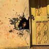在伊拉克安巴尔省拉马迪的一所学校，一个女孩通过冲突在墙壁上造成的破洞往外看。