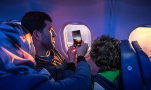 Des passagers regardent par le hublot de leur avion et prennent des photos lors de leur voyage de réinstallation.