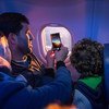 Una familia mira por la ventana del avión y toma fotos mientras viajan a su nuevo hogar. 