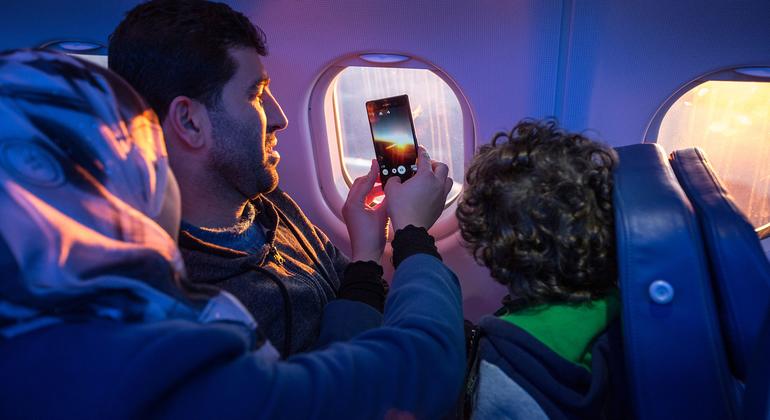 Una familia mira por la ventana del avión y toma fotos mientras viajan a su nuevo hogar. 