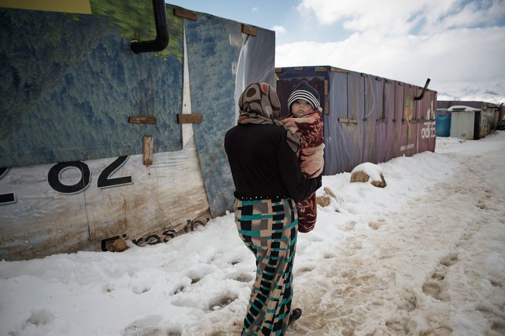 امرأة تحمل طفل رضيع وسط الثلوج في مخيم للاجئين بوادي البقاع، لبنان. Photo: UNICEF/UNI179012/Alessio Romenzi