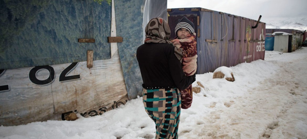 امرأة تحمل طفل رضيع وسط الثلوج في مخيم للاجئين بوادي البقاع، لبنان.