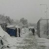Des gens traversent un camp de réfugiés enneigé, composé de tentes et de barbelés.