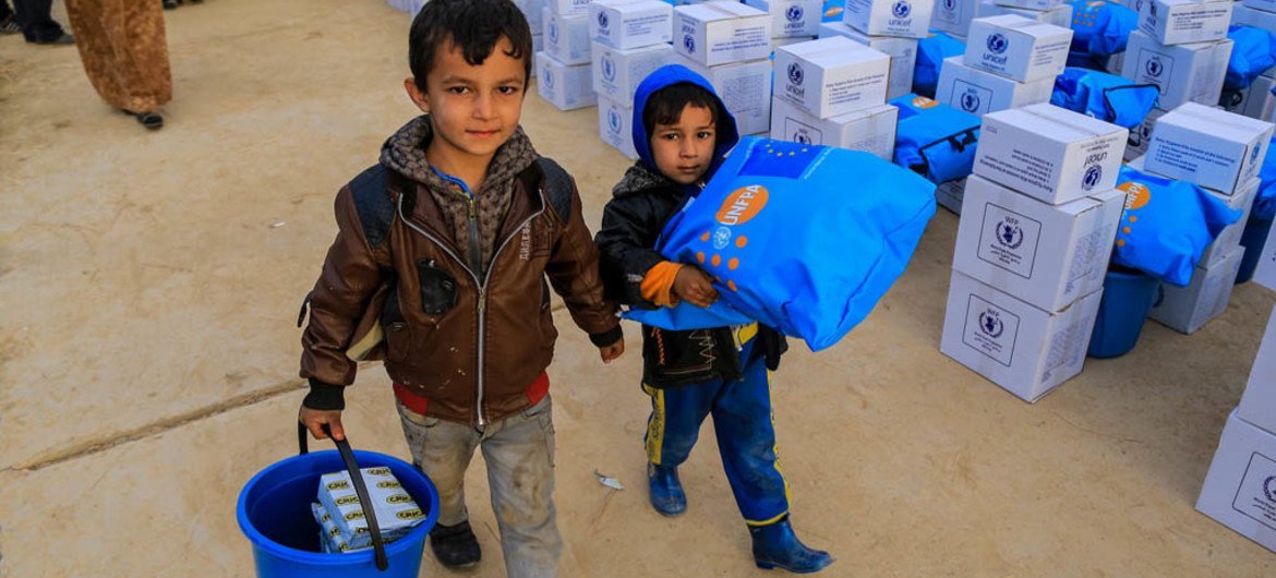 Айман (слева) и Халид (справа)   несут  товары, полученные  в центре по  распределению помощи в восточной части города Мосула в Ираке. Фото ЮНИСЕФ