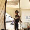 A young boy stands at the entrance of a UNHCR tent in a refugee camp.