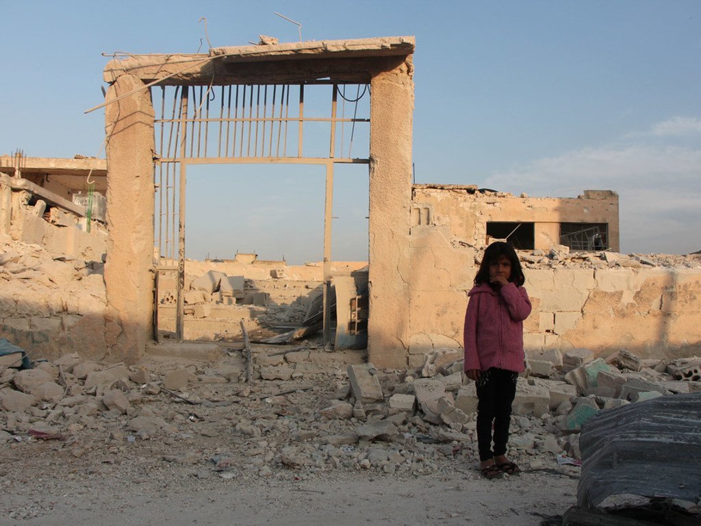 一名7岁的叙利亚女孩儿站在伊德利卜一所残破的学校前面。