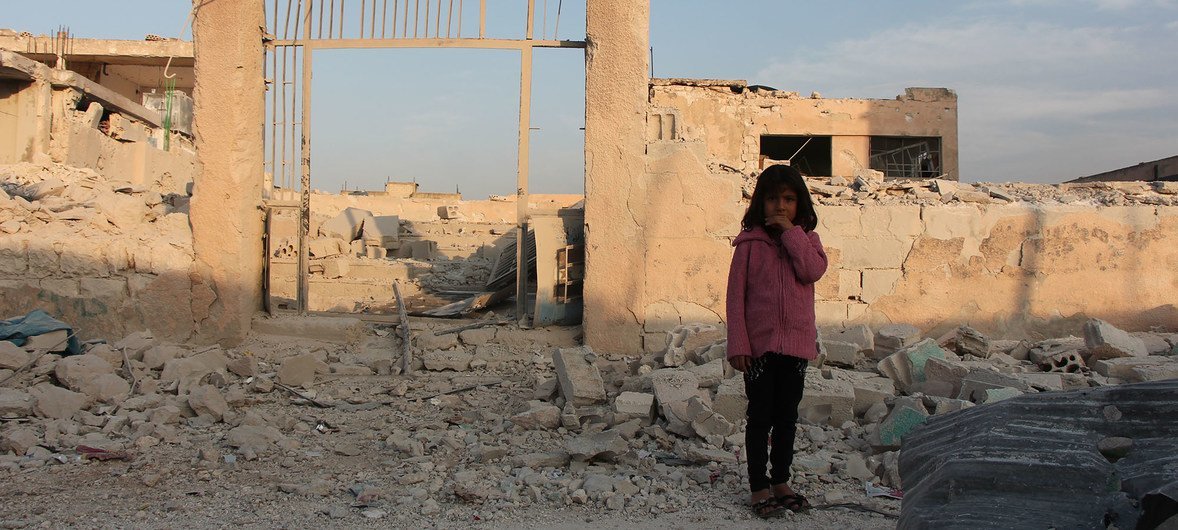 一名7岁叙利亚女孩儿站在伊德利卜的一座遭受破坏的学校前面。图片提供：儿基会