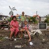 梅里安尼和她的孩子们坐在他们在斐济的家的砖墙上。他们的房子离海岸线只有几米远，在温斯顿飓风高度的强风暴潮中遭受了巨大的破坏。