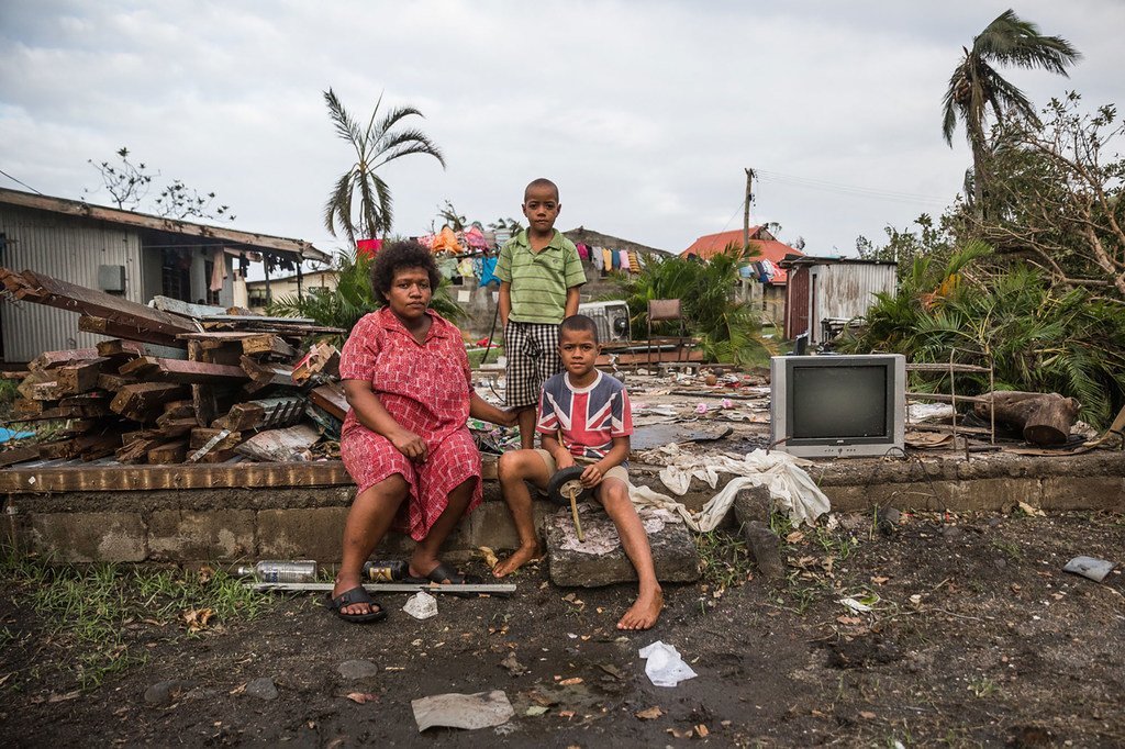 梅里安尼和她的孩子们坐在他们在斐济的家的砖墙上。他们的房子离海岸线只有几米远，在温斯顿飓风高度的强风暴潮中遭受了巨大的破坏。