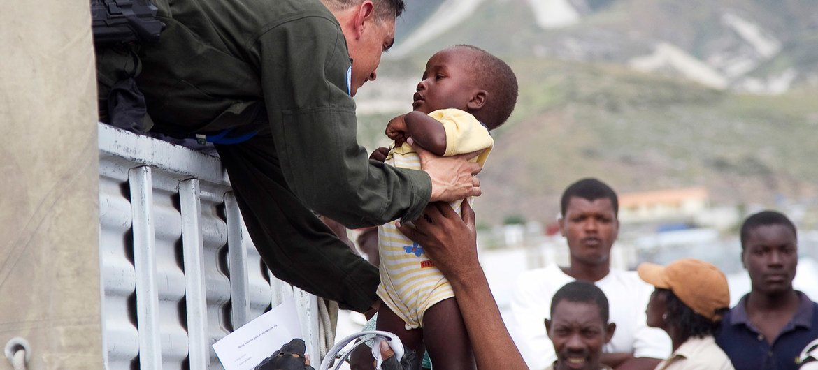 A UN peacekeeper helps a child aboard a truck during the relocation of residents of a camp for displaced persons.