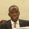 A Black man wearing glasses and a pinstripe suit speaks into a microphone at a conference.