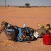 A peacekeeper in camouflage and protective gear lies on red sand while using a shovel for demining operations.