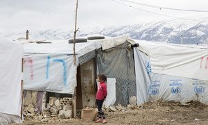 A Syrian refugee girl wears pink plastic slippers as she stands in front of shelters in an informal settlement in Ghazzeh, Bekaa, Lebanon as snow covers the mountains surrounding the valley.