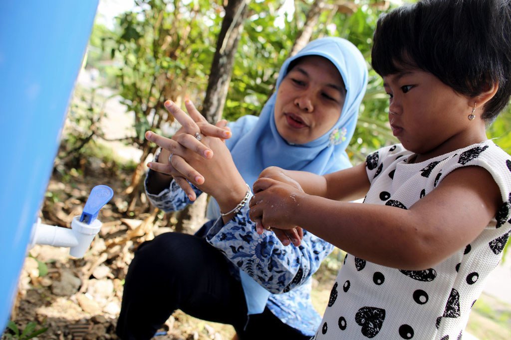 A volunteer community health worker shows a child how to wash her hands properly with soap, at an outdoor tap at the local community health post in Klaten District, Central Java Province, Indonesia.