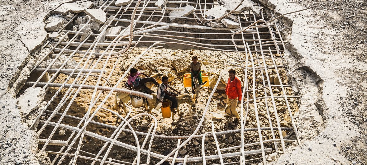 在也门的港口城市荷台达，一名男子和他的孩子穿过被空袭炸毁的废墟前去取水。