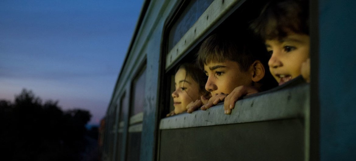 在前南斯拉夫的马其顿共和国，三名儿童从一辆载满叙利亚、阿富汗和伊拉克难民和移民的火车窗口向外望去。