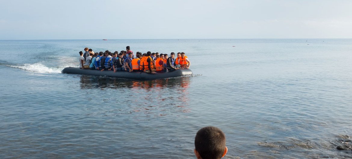 在希腊北爱琴海地区莱斯博斯岛，一名男孩从岸边看着一艘载满难民的大型橡皮艇正在靠近。