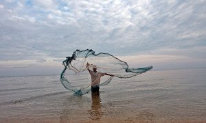 Fisherman in Timor Leste casts net in the water to catch small fish.