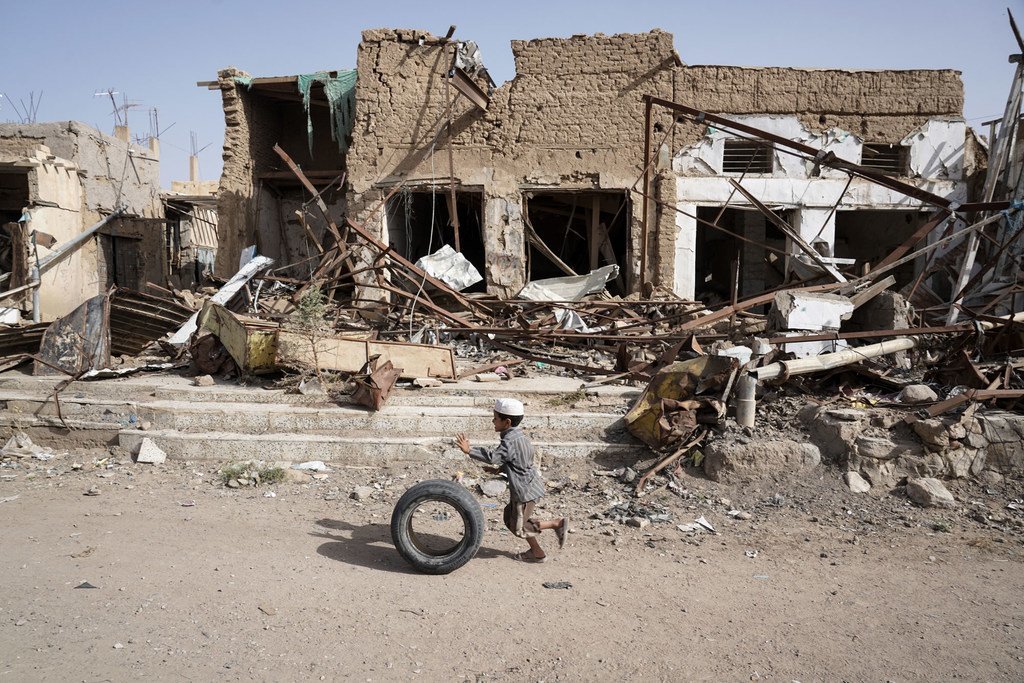 也门萨达老城，一名男童滚着轮胎从已成废墟的房屋跟前经过。