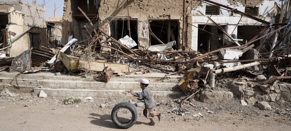 A young boy runs with his tyre past buildings damaged by air strikes in Saada Old Town.