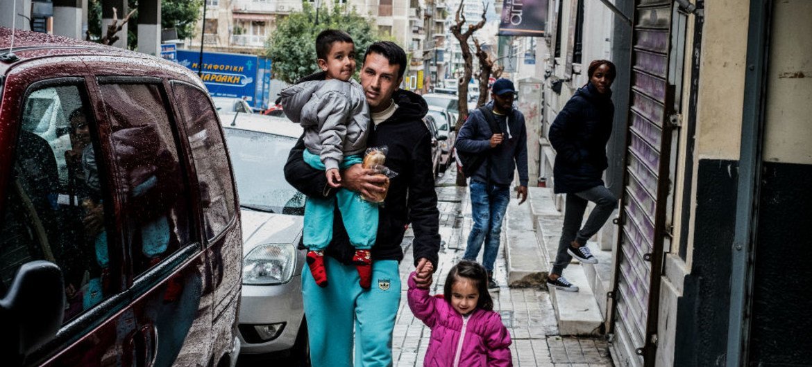 一名阿富汗难民带着自己的两个孩子从希腊雅典一家难民学习中心门外经过。