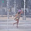 一名女孩儿在城市夏季高温中享受喷泉水流。