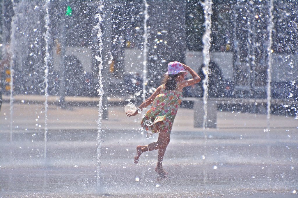 一名女孩儿在城市夏季高温中享受喷泉水流。