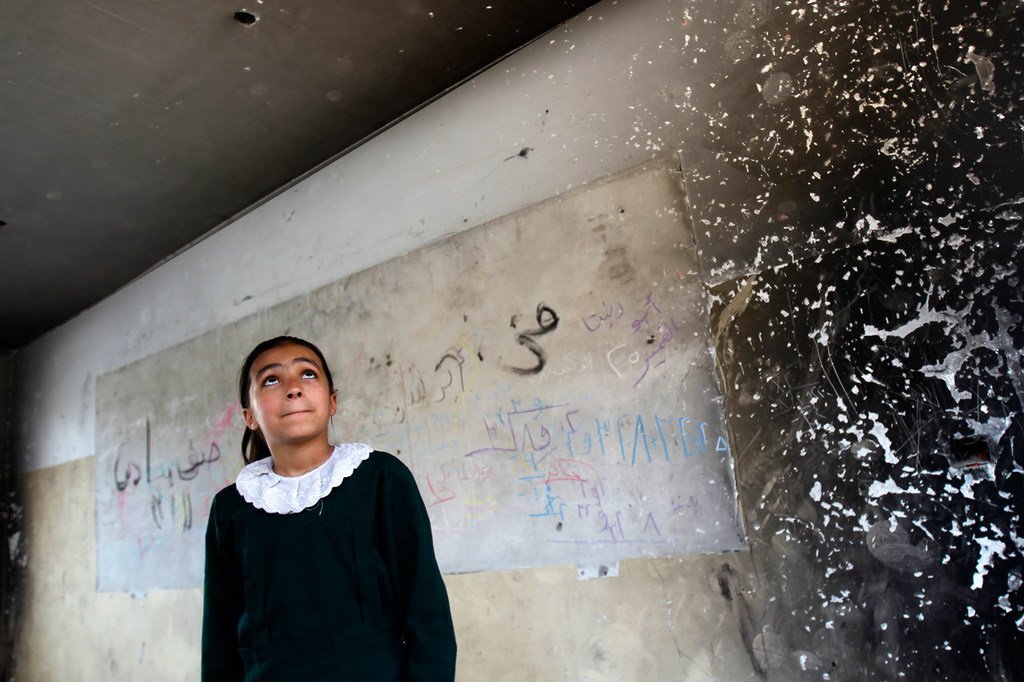 طالبة من الأراضي الفلسطينية المحتلة ، تنظر إلى الدمار الذي حصل لفصلها الدراسي خلال الأعمال القتالية عام 2014 في عزة.