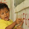 Un jeune garçon indique la lettre F, avec l'aide de son enseignant dans une école rurale au Népal.