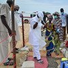 Health workers and medical staff at a field hospital in Nigeria treating a child during a cholera outbreak, with an ambulance and tents in the background.
