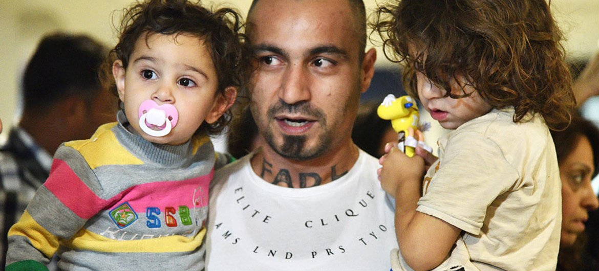 Un padre sirio cargando a sus dos hijos a su llegada al aeropuerto internacional de Santigo de Chile.