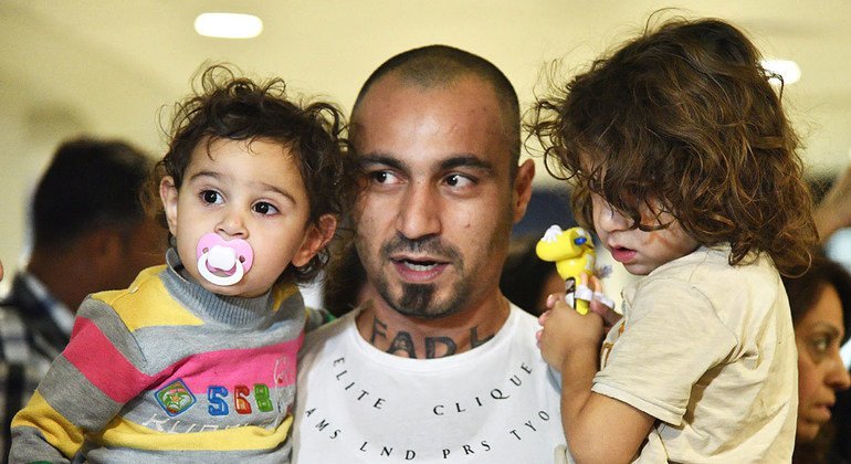 Un padre sirio cargando a sus dos hijos a su llegada al aeropuerto internacional de Santigo de Chile. 