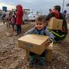 在伊拉克库尔德斯坦地区埃尔比勒省的卡沃格斯科叙利亚难民营，一名三岁的男童坐在一箱冬衣上，这是他的家人从分发处领到的。