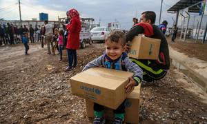 A three-year-old boy sits on a box of winter clothing that his family has received from a distribution at Kawergosk Syrian Refugee Camp in Erbil Governorate in the Kurdistan region of Iraq.