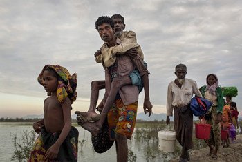Rohingya refugees who crossed the Naf River, which demarcates the border between Myanmar and Bangladesh, on makeshift rafts made of logs, bamboo poles and jerrycans, walk along an embankment.
